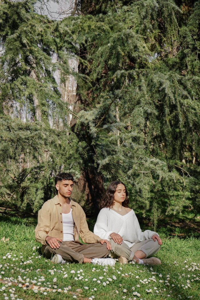 A man and woman meditating outdoors in a tranquil forest environment, embodying relaxation and mindfulness.