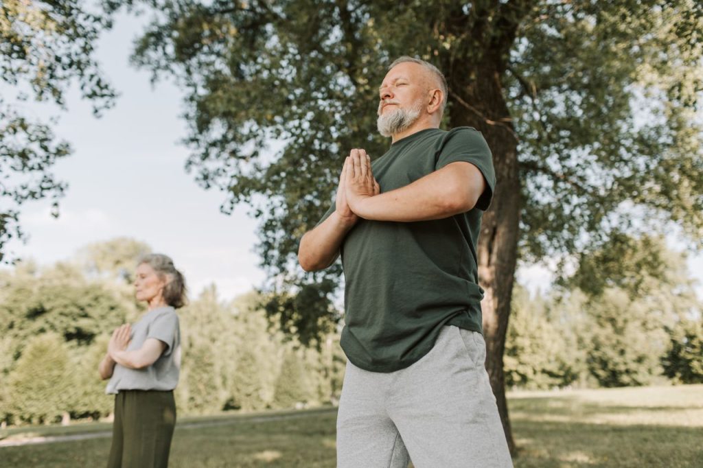Elderly couple meditating in a peaceful park setting, promoting a healthy lifestyle.