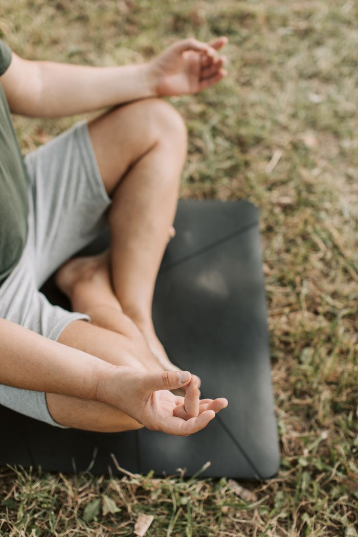 Person practicing meditation in lotus pose outdoors on a yoga mat.